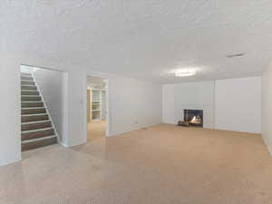 Finished basement with stairs, light colored carpet, a textured ceiling, and a warm lit fireplace