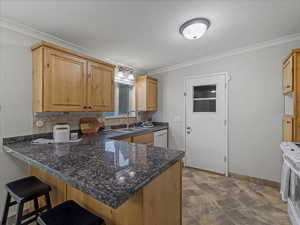 Kitchen featuring a peninsula, crown molding, dark countertops, a kitchen bar, and white appliances