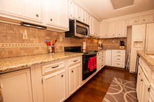 Kitchen featuring black electric range oven, white fridge with ice dispenser, dark wood-type flooring, light stone counters, and a textured ceiling