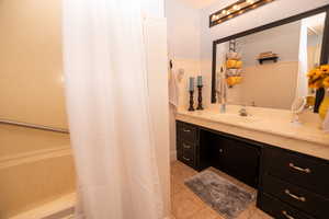 Bathroom featuring vanity, shower / bathtub combination with curtain, a wainscoted wall, and light tile patterned flooring