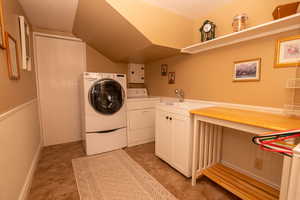 Washroom featuring washer and clothes dryer, cabinet space, lofted ceiling, and a wainscoted wall