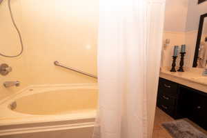 Bathroom with shower / tub combo with curtain, vanity, light tile patterned floors, and a wainscoted wall