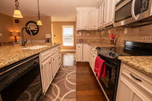 Kitchen with black appliances, dark wood finished floors, pendant lighting, light stone counters, and a textured ceiling