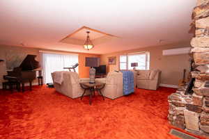 Carpeted living room with a fireplace, healthy amount of natural light, a raised ceiling, a textured ceiling, and a wall mounted air conditioner