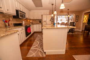 Kitchen featuring electric range, decorative light fixtures, a textured ceiling, light stone countertops, and backsplash