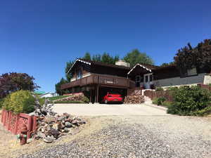 View of front of home featuring brick siding, a wooden deck, driveway, a chimney, and a carport