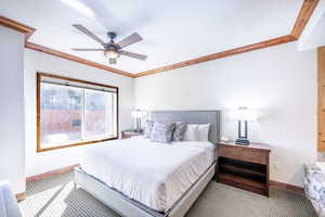 Carpeted bedroom with a textured wall, ceiling fan, ornamental molding, and a textured ceiling