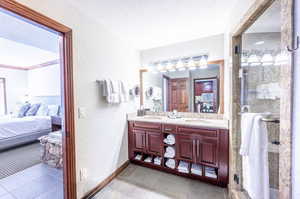 Bathroom featuring connected bathroom, a textured wall, double vanity, a textured ceiling, and a stall shower