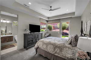 Carpeted bedroom featuring ceiling fan, recessed lighting, a tray ceiling, access to exterior, and ensuite bathroom