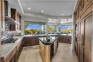 Kitchen featuring a center island, wall chimney exhaust hood, decorative light fixtures, decorative backsplash, and recessed lighting