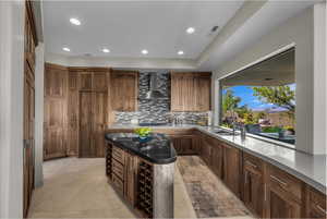 Bar area with recessed lighting, wall chimney range hood, tasteful backsplash, dark stone countertops, and dark brown cabinetry
