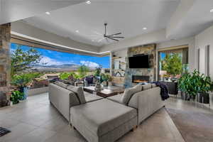 Living area with a stone fireplace, a ceiling fan, built in shelves, recessed lighting, and tile patterned floors