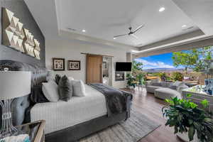 Bedroom with a raised ceiling, a barn door, wood-type flooring, connected bathroom, and recessed lighting