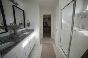 Ensuite bathroom featuring double vanity, a walk in closet, a shower stall, and light tile patterned floors