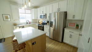 Kitchen featuring a quartz kitchen island, appliances with stainless steel finishes, white cabinetry, and light stone counters