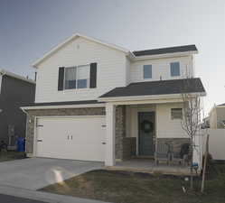 View of front of house featuring stone siding, driveway, an attached garage, and covered porch