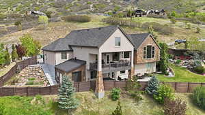 Rear view of house featuring a balcony, stucco siding, a fenced backyard, a shingled roof, and stone siding