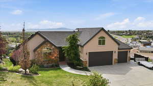 View of front of property featuring stone siding, roof with shingles, stucco siding, driveway, and a front yard