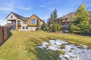 Back of house with stucco siding, stone siding, solar panels, and a balcony