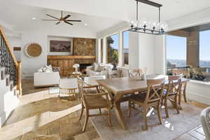 Dining area featuring stone tile floors, stairway, a lit fireplace, lofted ceiling, and a ceiling fan