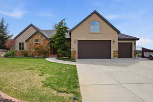 View of front of home featuring stucco siding, stone siding, a front yard, and driveway