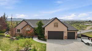 View of front facade with stone siding, stucco siding, a garage, and a mountain view