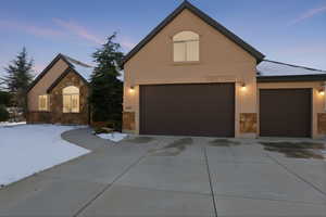 View of front of home with stone siding, stucco siding, a garage, and driveway