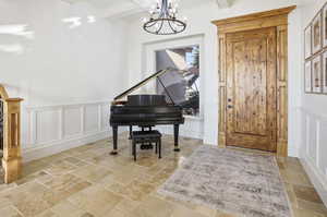 Foyer with a decorative wall, a wainscoted wall, stone tile flooring, beamed ceiling, and a chandelier