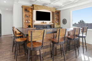 Indoor wet bar with dark countertops, open shelves, dark wood-type flooring, coffered ceiling, and beamed ceiling