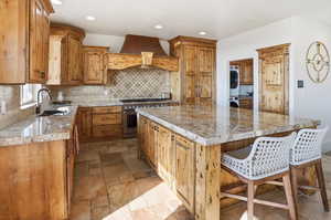 Kitchen featuring a kitchen breakfast bar, high end range, a kitchen island, decorative backsplash, and premium range hood