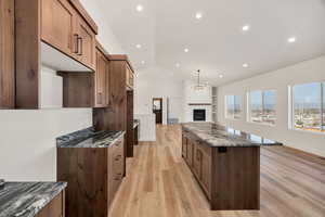 Kitchen with dark stone countertops, a kitchen island, light wood-type flooring, a fireplace, and recessed lighting