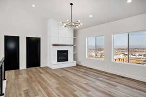 Unfurnished living room featuring light wood-style flooring, a chandelier, a large fireplace, recessed lighting, and lofted ceiling
