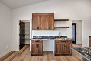 Kitchen featuring open shelves, dark stone counters, brown cabinetry, lofted ceiling, and light wood-style flooring