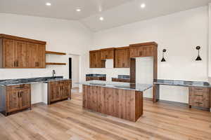 Kitchen with brown cabinetry, dark stone countertops, open shelves, high vaulted ceiling, and a center island