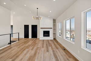 Unfurnished living room with built in features, a chandelier, light wood-style floors, recessed lighting, and a large fireplace