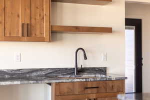 Kitchen featuring open shelves, brown cabinetry, and dark stone counters