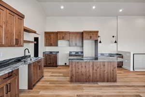 Kitchen with dark stone countertops, brown cabinetry, open shelves, light wood finished floors, and recessed lighting