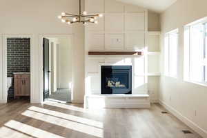Unfurnished living room featuring a glass covered fireplace, wood finished floors, hanging lights, and vaulted ceiling