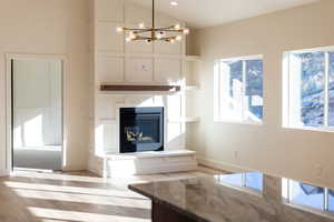 Unfurnished living room with healthy amount of natural light, a multi sided fireplace, wood finished floors, hanging lights, and vaulted ceiling