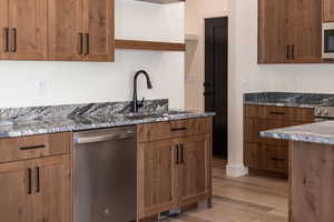 Kitchen with stainless steel dishwasher, dark stone counters, open shelves, light wood finished floors, and wood finish cabinets