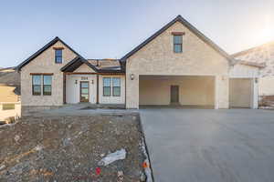 View of front facade with stone siding, driveway, and board and batten siding