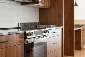 Kitchen featuring electric range, wood finish cabinets, light stone countertops, and modern cabinets