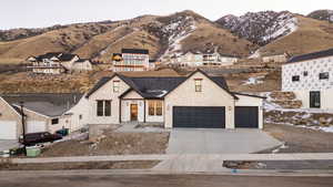 View of front of property featuring concrete driveway, a garage, a mountain view, stone siding, and a residential view