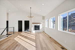 Unfurnished living room featuring a glass covered fireplace, light wood-type flooring, suspended lighting, and vaulted ceiling