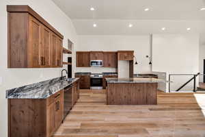 Kitchen featuring dark stone counters, lofted ceiling, light wood-style floors, stainless steel appliances, and a kitchen island
