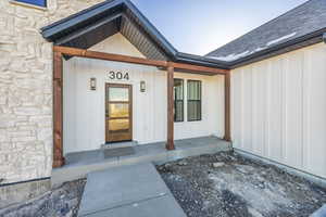 Property entrance featuring board and batten siding, stone siding, roof with shingles, and covered porch