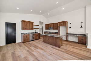 Kitchen with dark stone countertops, open shelves, light wood-type flooring, stainless steel appliances, and a kitchen island