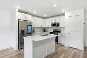 Kitchen featuring white cabinets, appliances with stainless steel finishes, a kitchen island with sink, light wood finished floors, and recessed lighting