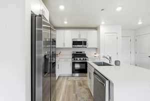 Kitchen with appliances with stainless steel finishes, white cabinets, an island with sink, light wood-style floors, and light stone countertops
