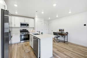 Kitchen featuring stainless steel appliances, white cabinets, an island with sink, light wood finished floors, and recessed lighting